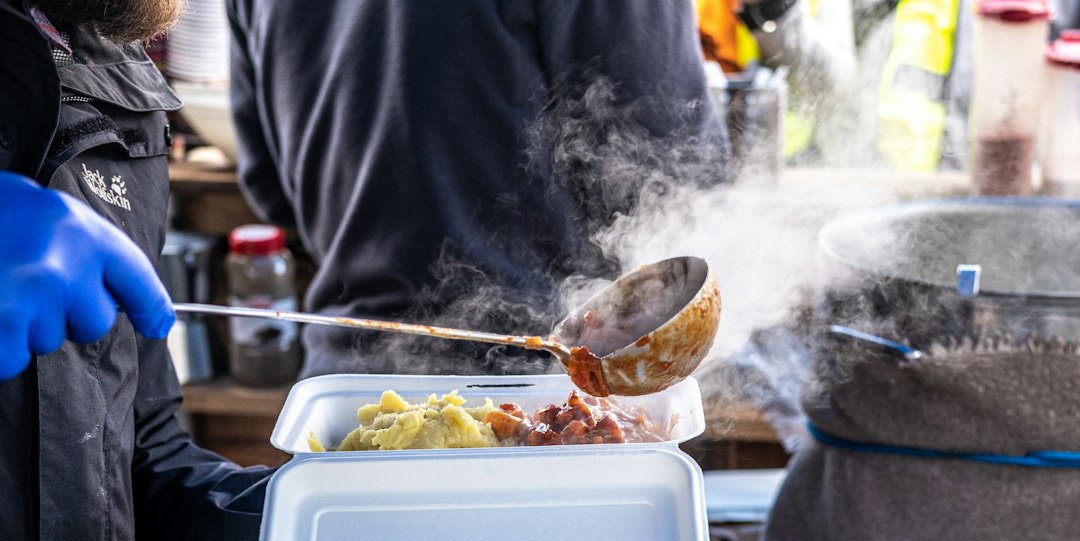A person in blue gloves stirring food in a container