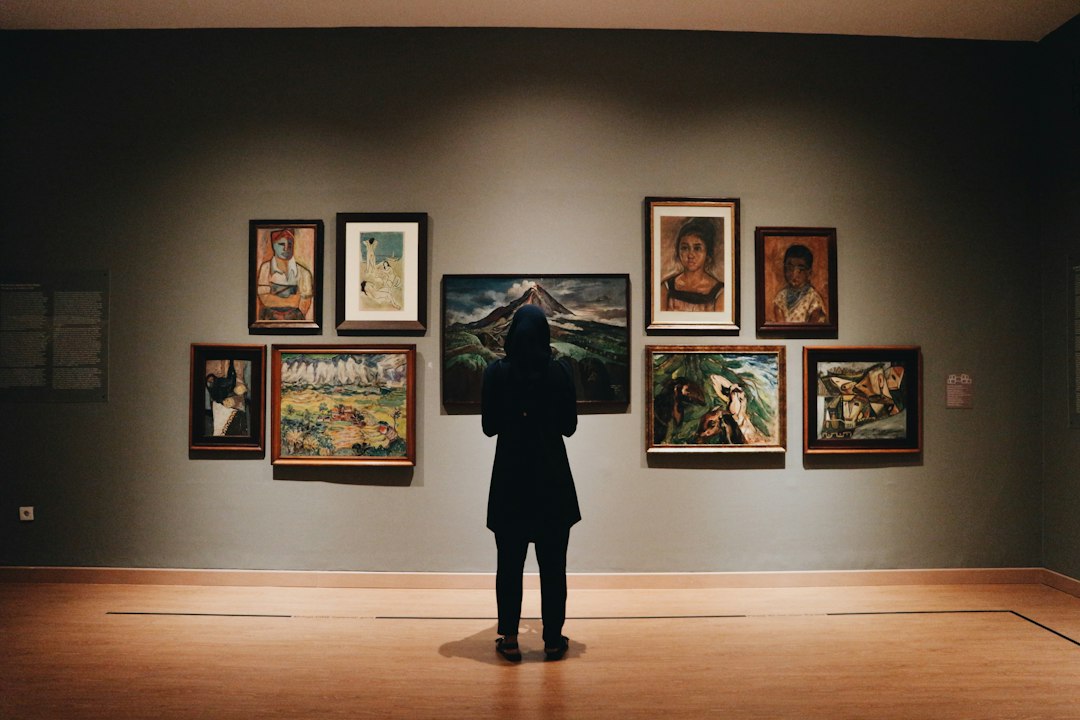 A woman in a black coat standing in front of framed paintings in a gallery