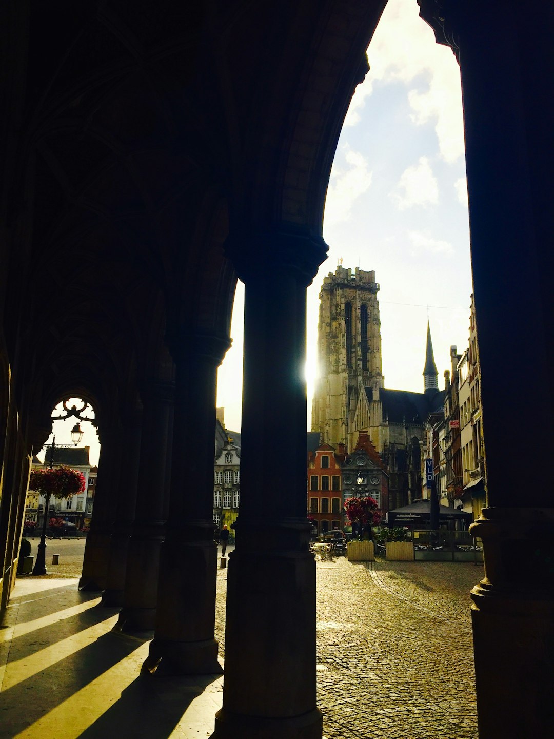 Stone arcade framing St. Rumbold's Tower and the old town of Mechelen, Belgium, in morning light