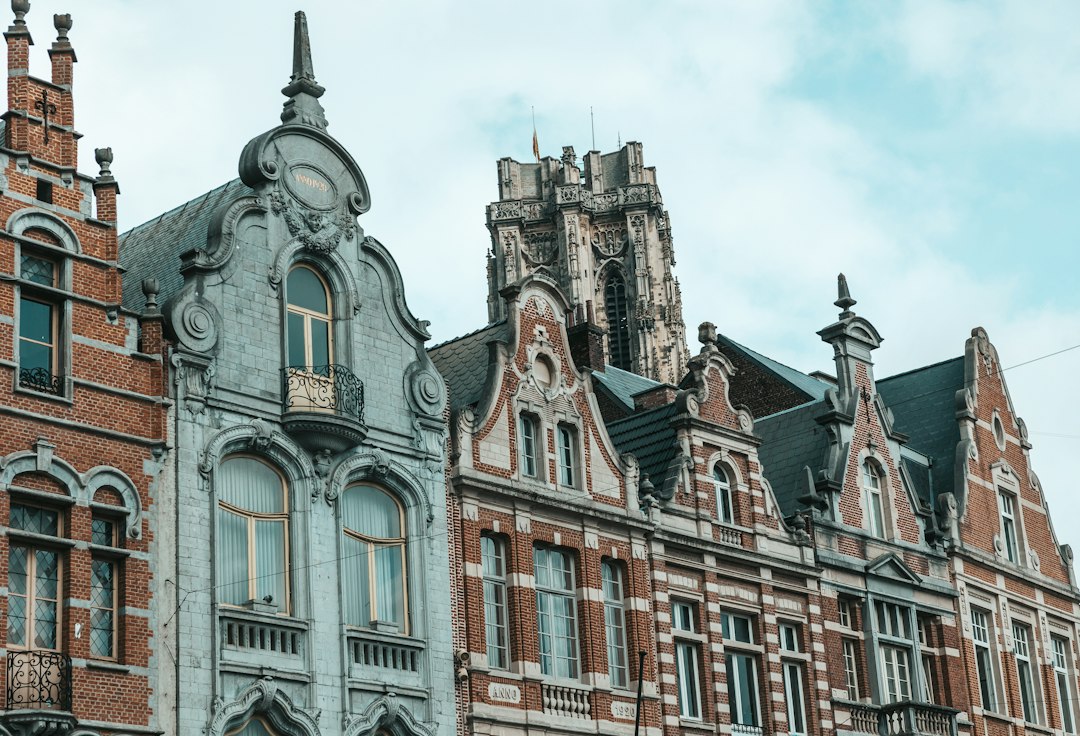 Ornate brick and stone gabled townhouses with St. Rumbold's Tower rising behind them in Mechelen, Belgium