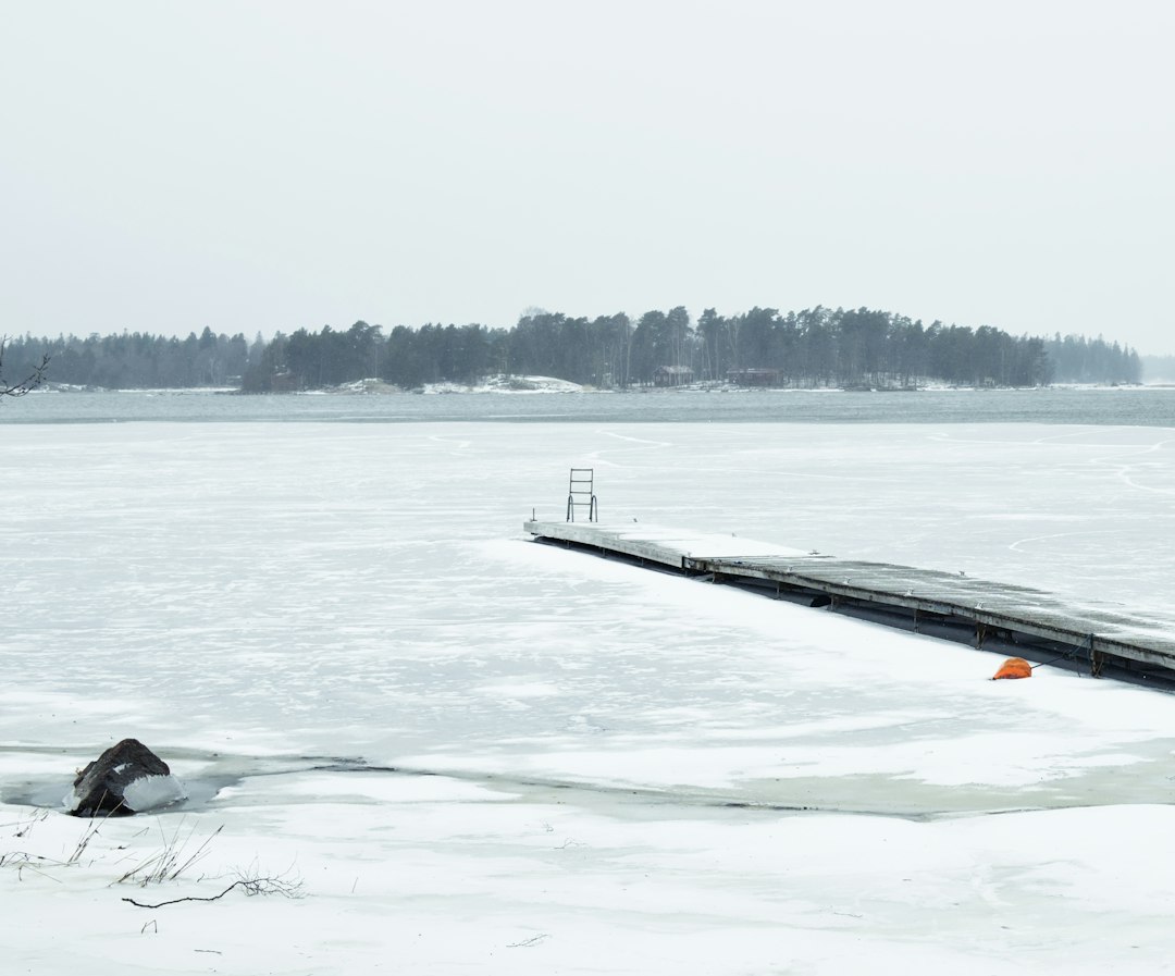 Wooden sauna hut and jetty beside a partly frozen lake at dusk with steam rising
