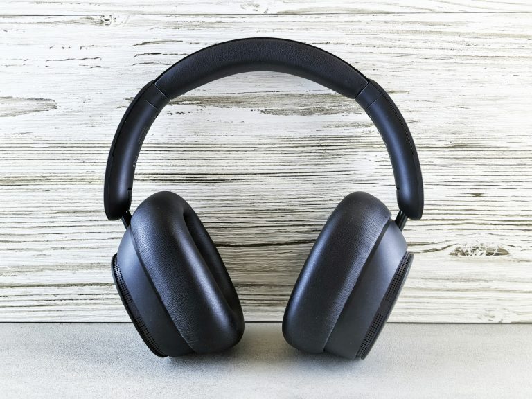Black over-ear wireless headphones standing upright against a white-washed wooden wall