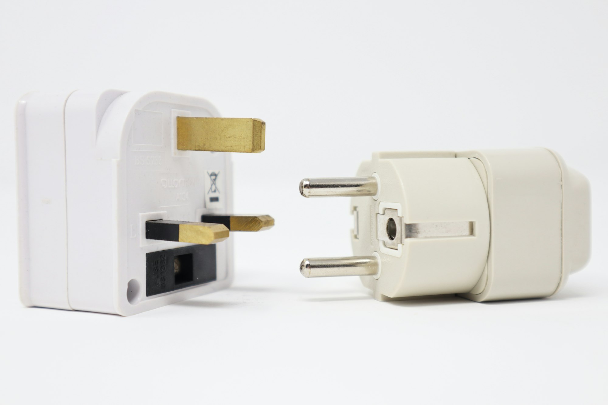 Two white travel plug adapters with different pin shapes standing side by side on a white surface