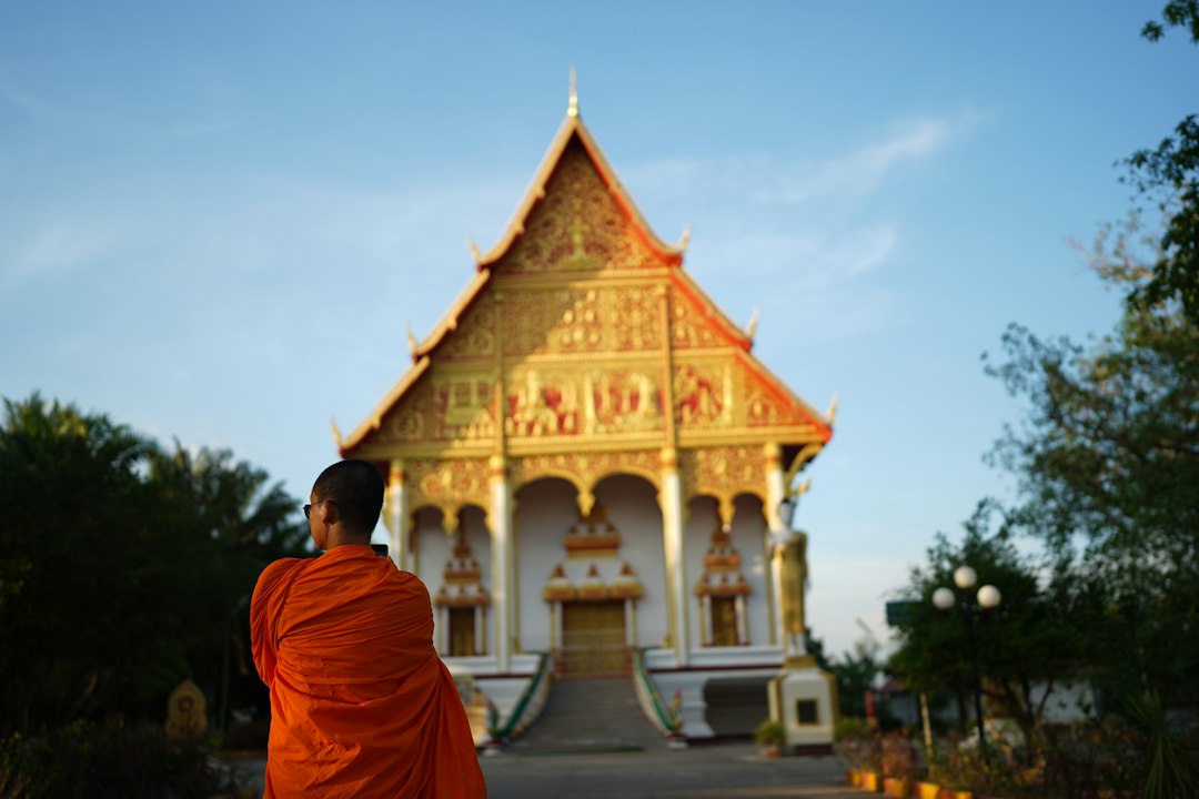 A person in an orange robe standing in front of a building in Vientiane, Laos